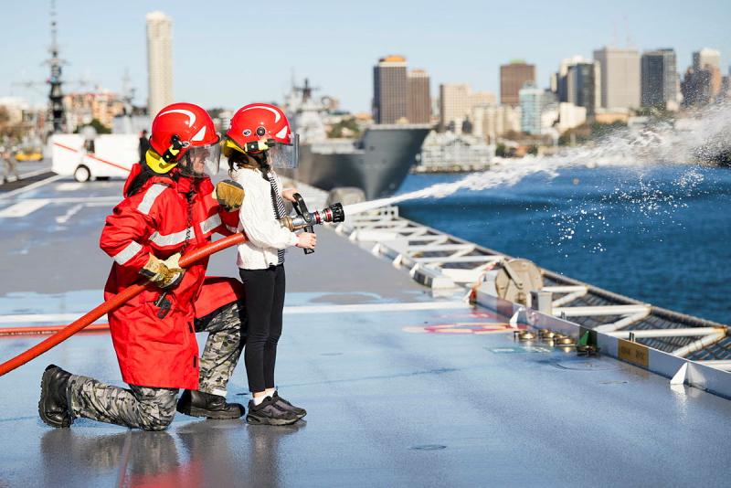 An adult and a child use a fire hose on a ship.