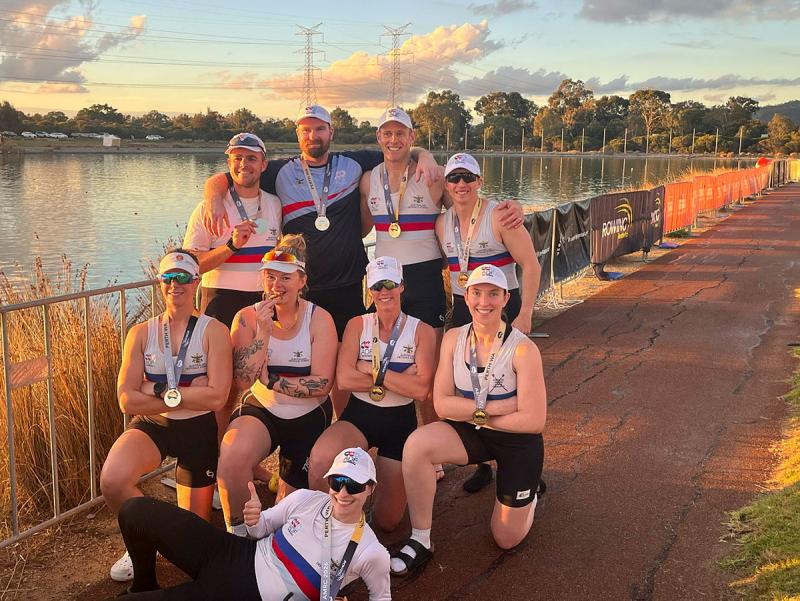 A group of men and women with medals stand by a lake.