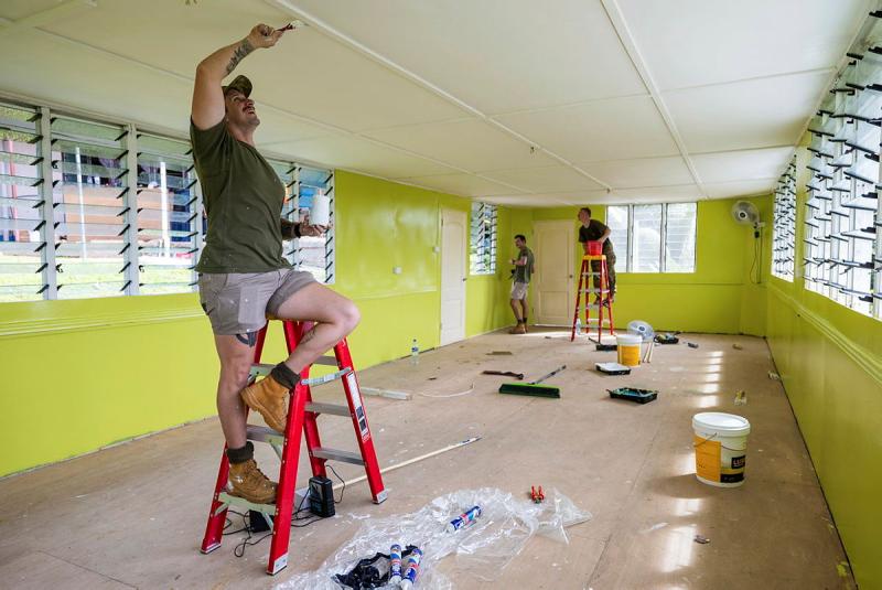 A man paints the ceiling while standing on a small step ladder.