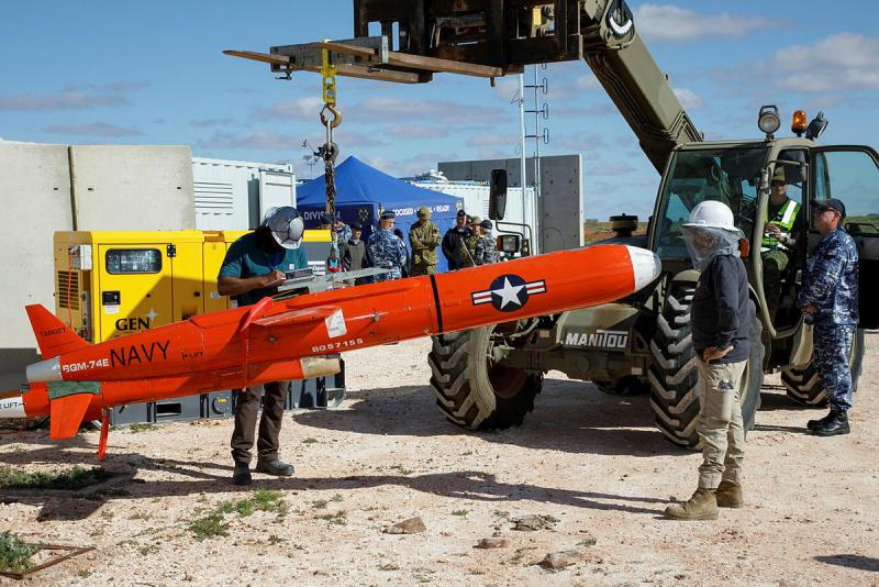 Several men transport a red Navy missile by a miniature crane.