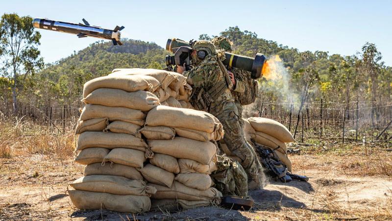 A soldier fire a missile from behind a wall of sand bags.