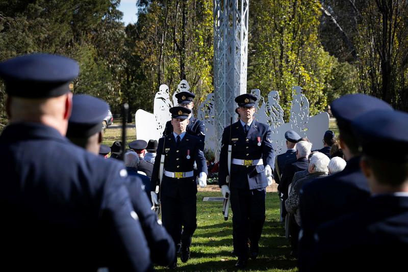 Armed military personnel walk in formation down an aisle of seated people.