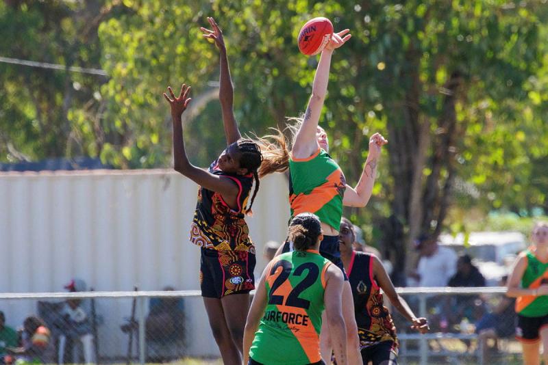 Two women jump and reach for a football.