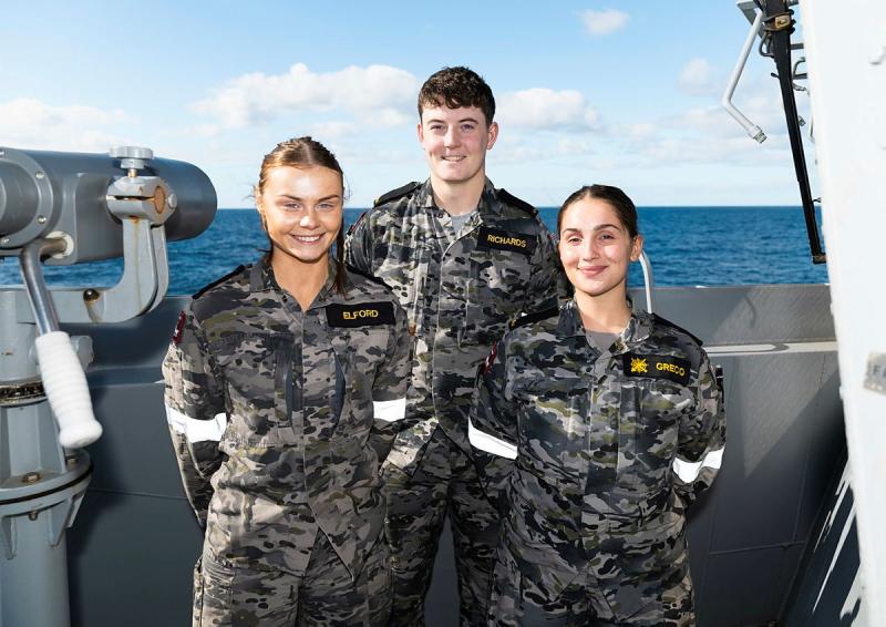 Three sailors pose together on a ship.