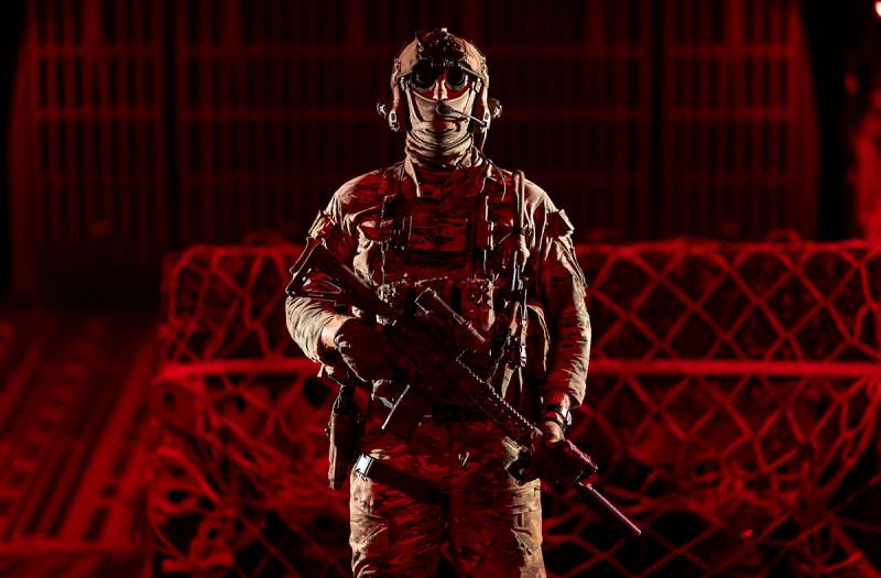 A man in combat uniform standing in the hull of an aircraft holding a rifle.