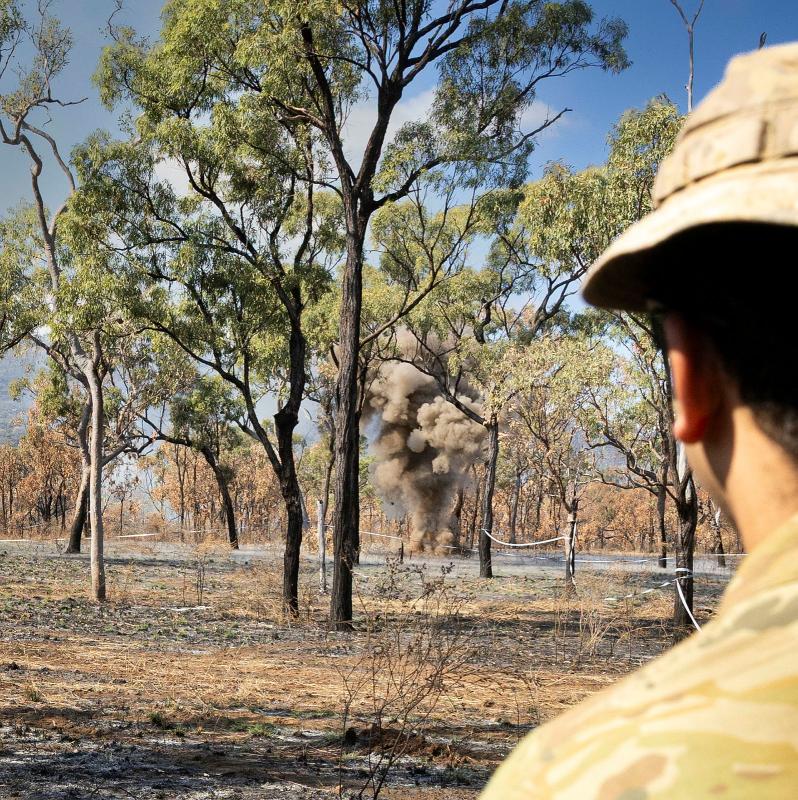 Shot from behind a soldier's ear of a blast in among trees.