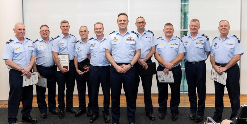 Nine men in Air Force uniforms standing together in a line while smiling and facing the camera.