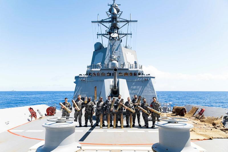 Sailors hold gun casings on a ship.