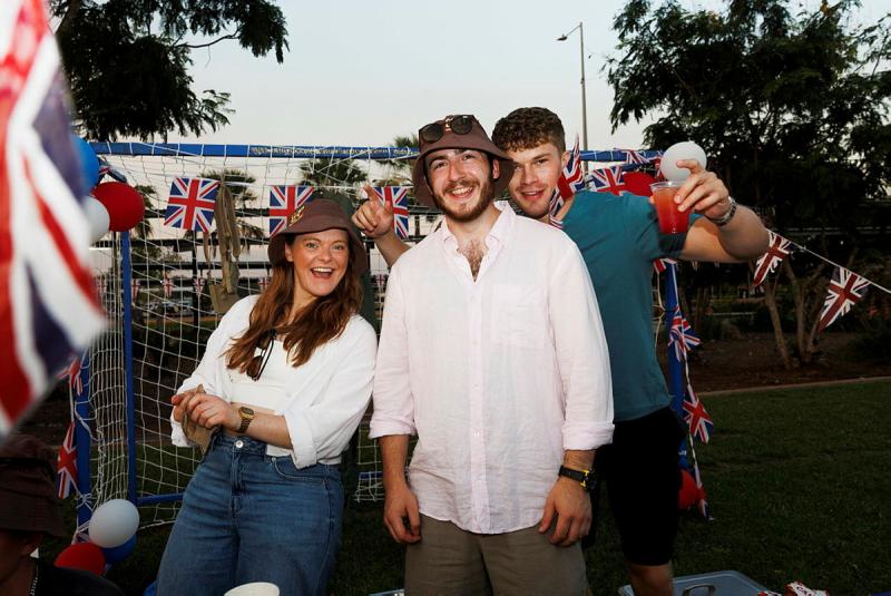 Three British people in patriotic paraphernalia stand before a soccer goal.