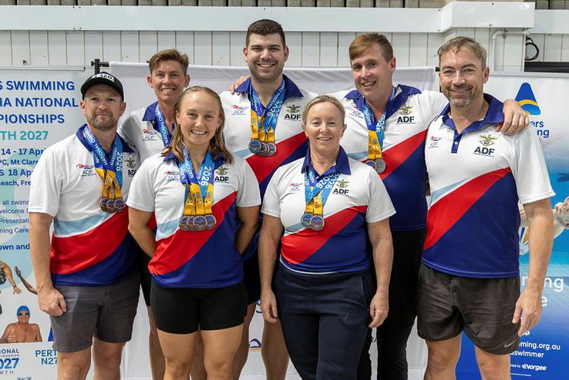 Navy personnel in their swim team uniforms stand in a group with medals around their necks