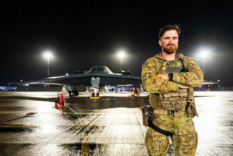 A man in military uniform stands on the tarmac in front of an aircraft.