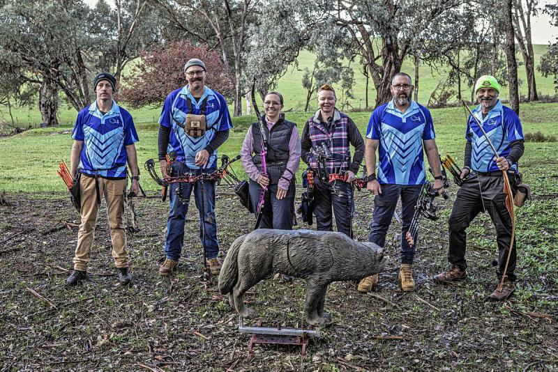 A group of archers in the same shirt stand next to a metal fox monument.
