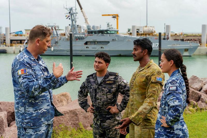 A man talks to three other people, all in military uniforms.