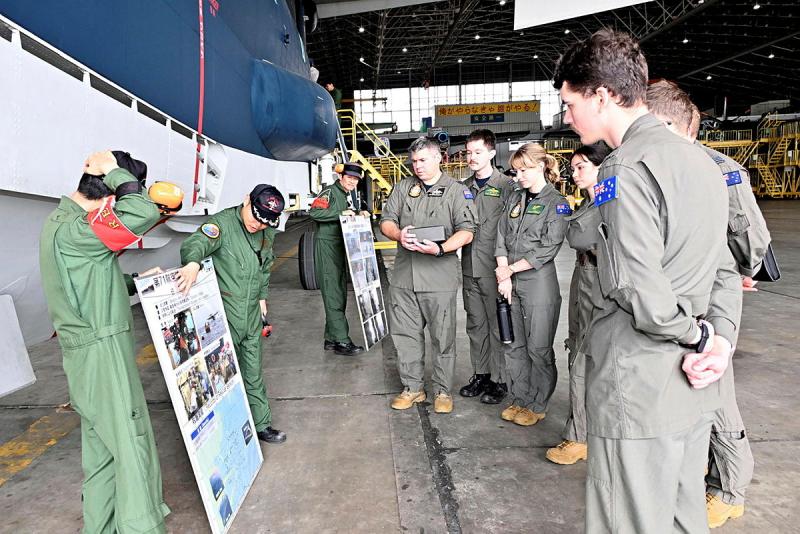 Military personnel standing around in an aircraft hangar.