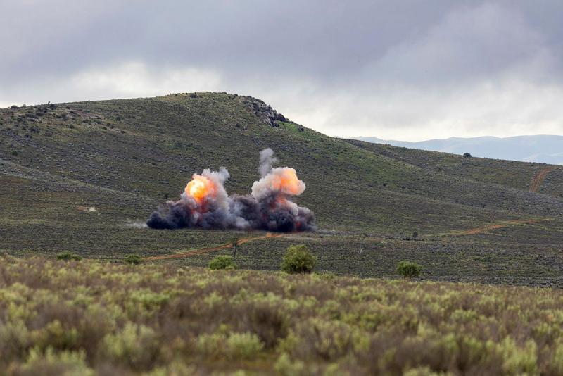 An explosion shows black smoke and orange flame in an open grassy area.