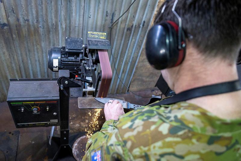 A military member sharpens a blade.