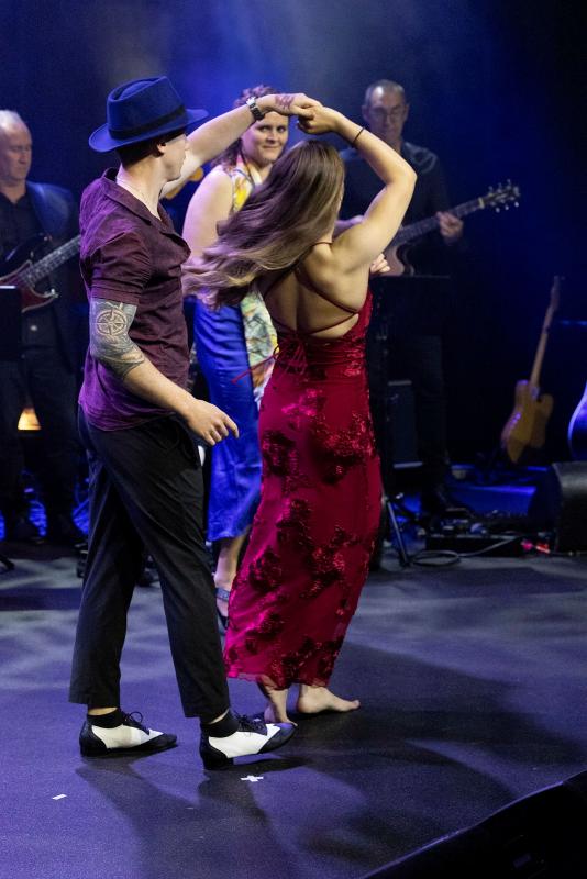 A man spins a woman while they dance in front of a band.