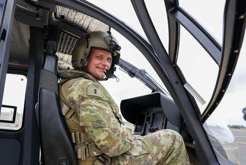 A military man sits inside the cockpit of a helicopter.