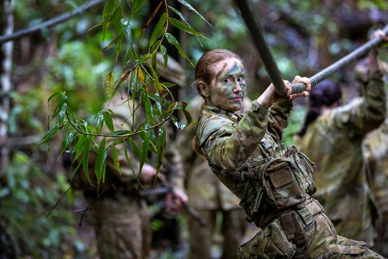 A woman in camouflage uniform and face paint moves along ropes in a jungle.