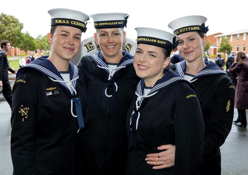 Four female sailors in Navy uniforms crowd together for a photo.
