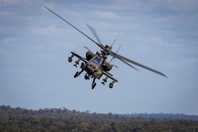 A military helicopter in flight over bush landscape.