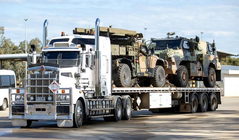 A large truck carries two smaller military vehicles.