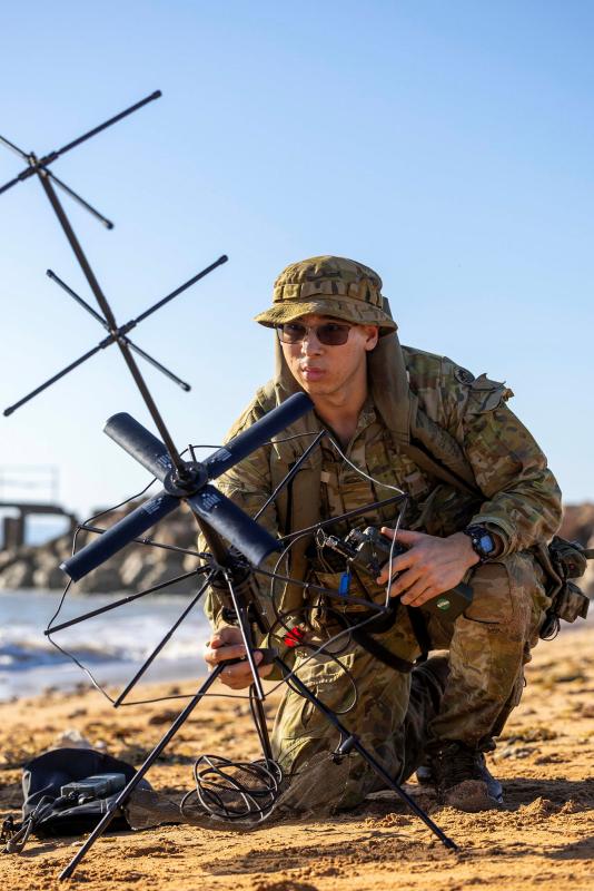 A military man sets up a signal device on a beach.