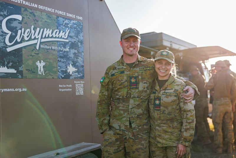 Two military members stand next to a truck with a sign titled 'Everyman's'.