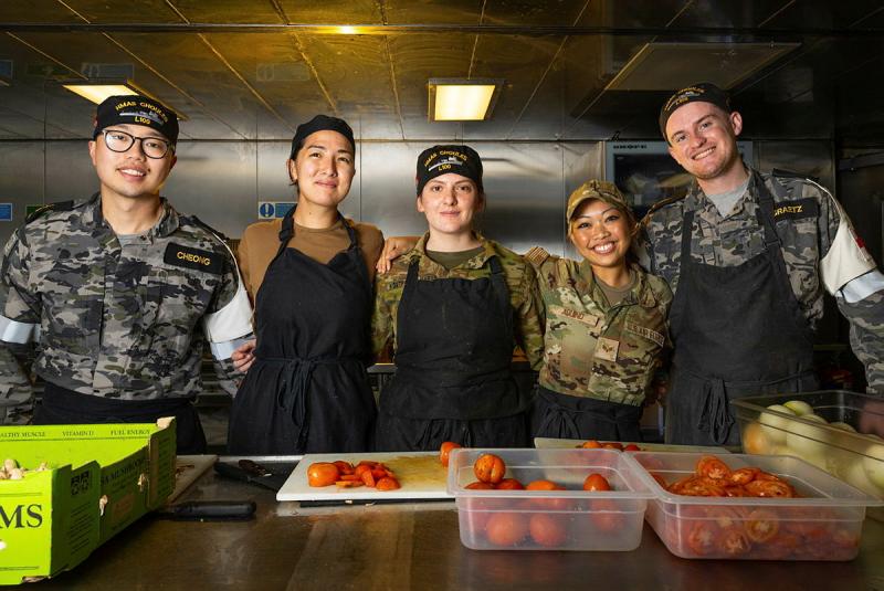 A group of military personnel standing together for a group photo in an industrial kitchen.