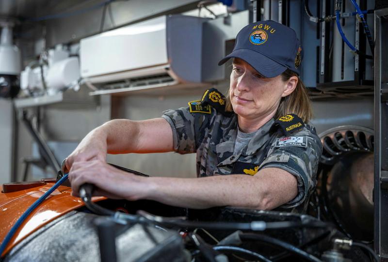 A sailor works on a piece of equipment, handling electrical cables.