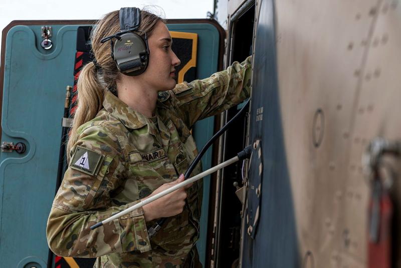 A soldier wearing ear protection reaches into the side of a helicopter.