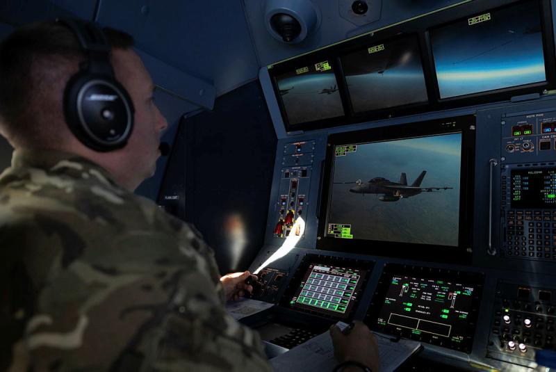 A military member looks at a handful of screens depicting the sky and an aircraft.
