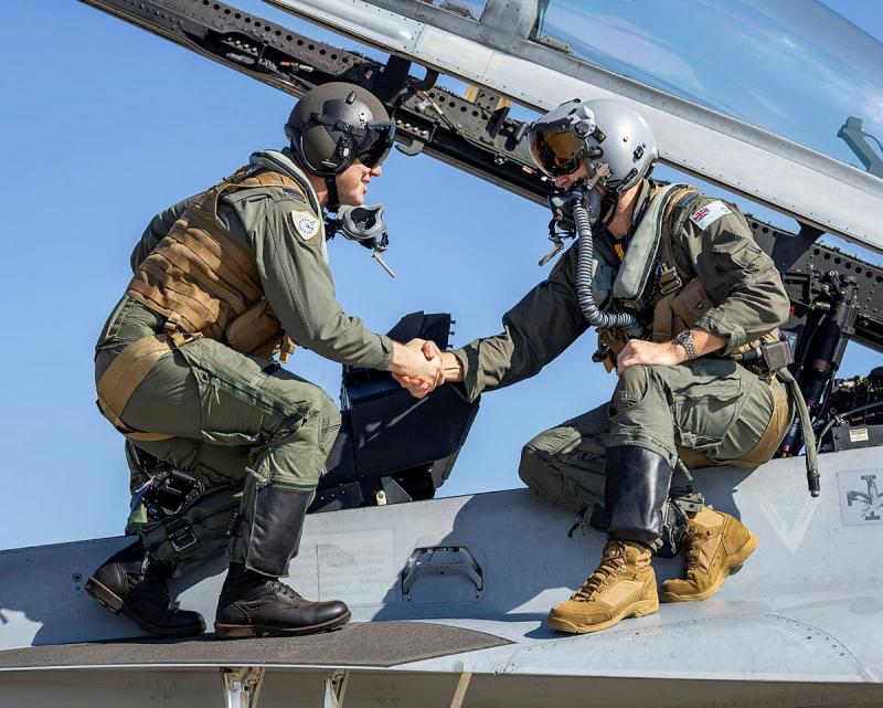 Two military aviators shake hands on top of an aircraft.