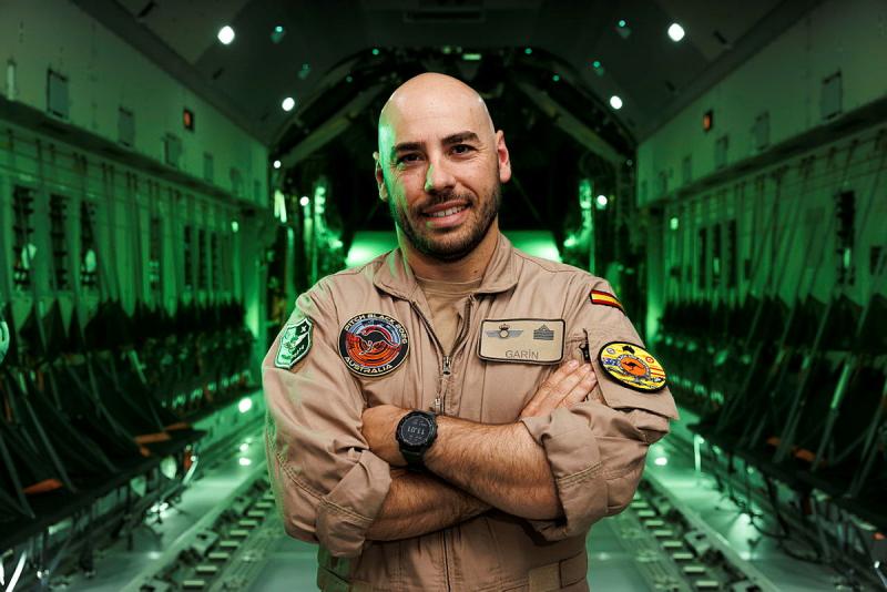 A military man with his arms across his chest inside an aircraft lit up in green.
