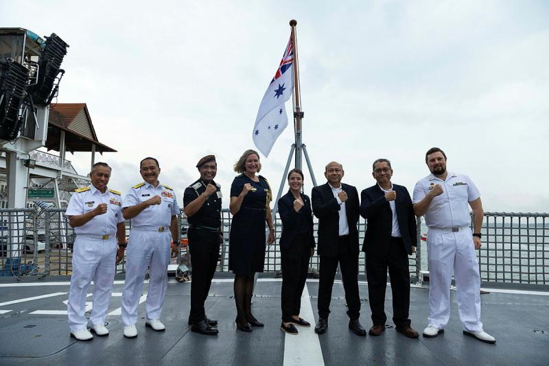 Malaysian and Australian officials and personnel stand in front of a flag fist pumping in unison.