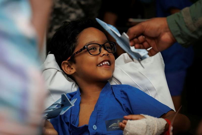 A child smiles to see a person (unseen) show him a miniature aircraft.