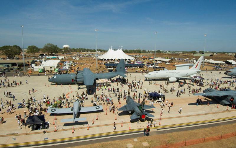A large crowd of people swarm around a collection of aircraft on a tarmac.
