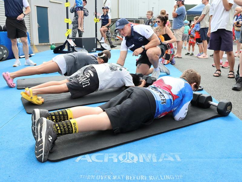 Civilain children do push ups while directed by a Navy personal trainer.