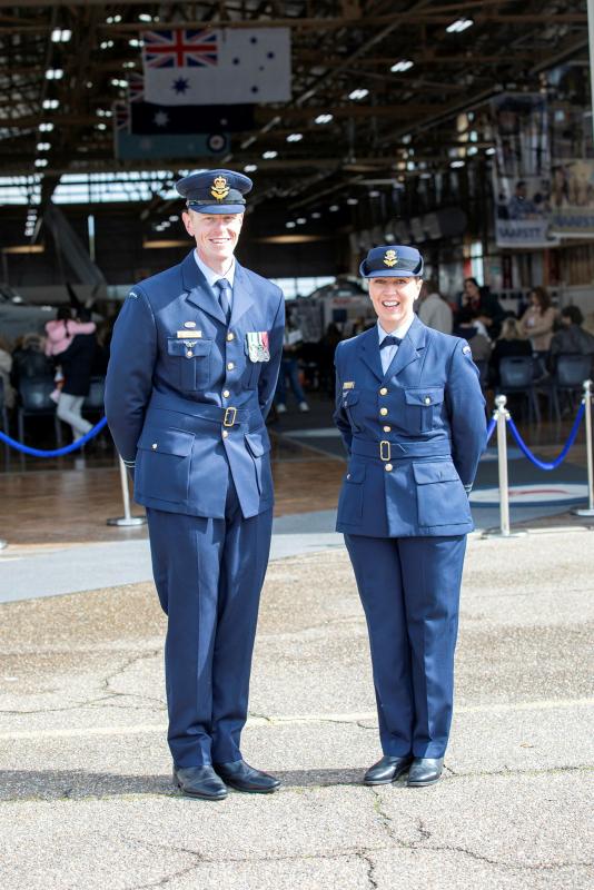 Two military members in front of a building of civilians and personnel.