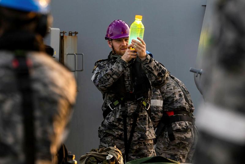 A sailor holds a bottle full of liquid p to eye level to inspect it.