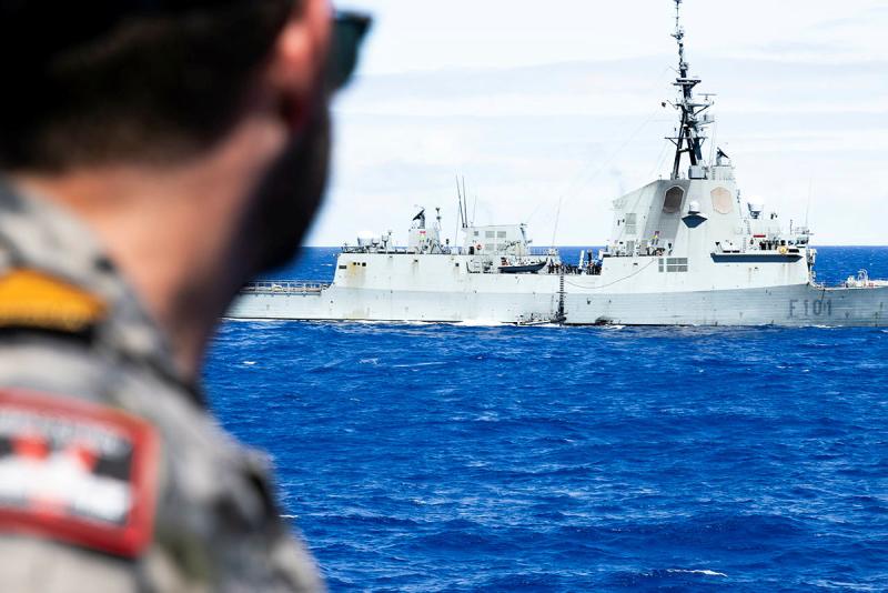 A military member looks out to sea at a ship.