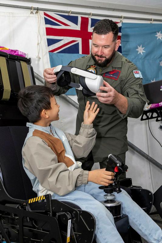 A military member puts a pair of VR goggles onto a young boy's head.