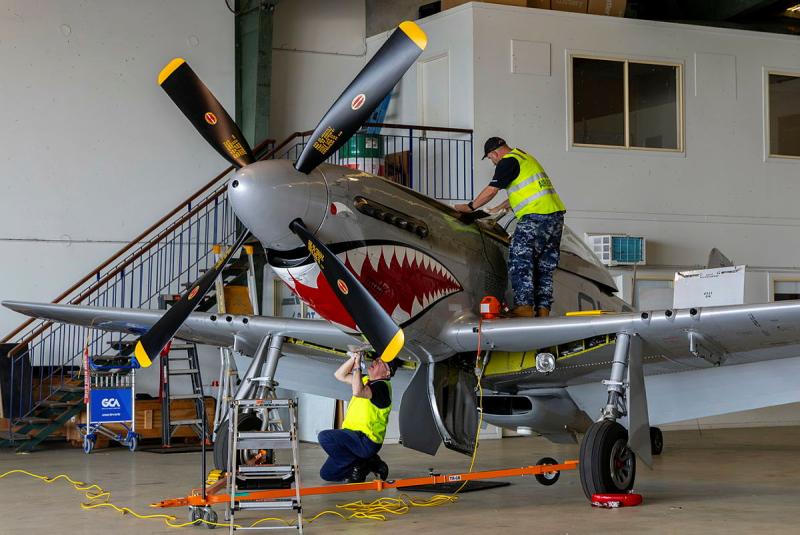 Two military personnel work on an aircraft decorated to look like a shark.