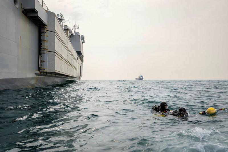 Three people swim next to a ship.