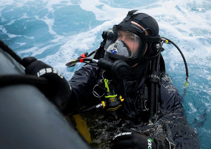 A diver hangs onto a ship. 