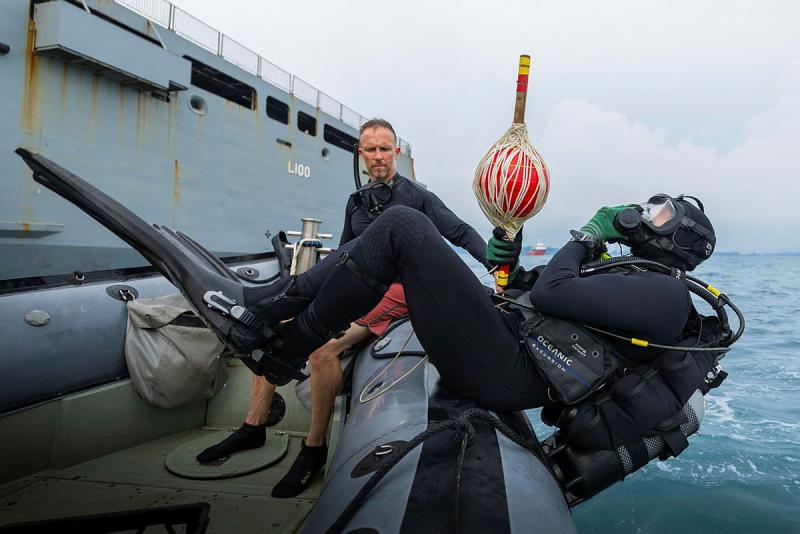 A diver back rolls off a boat into the water.