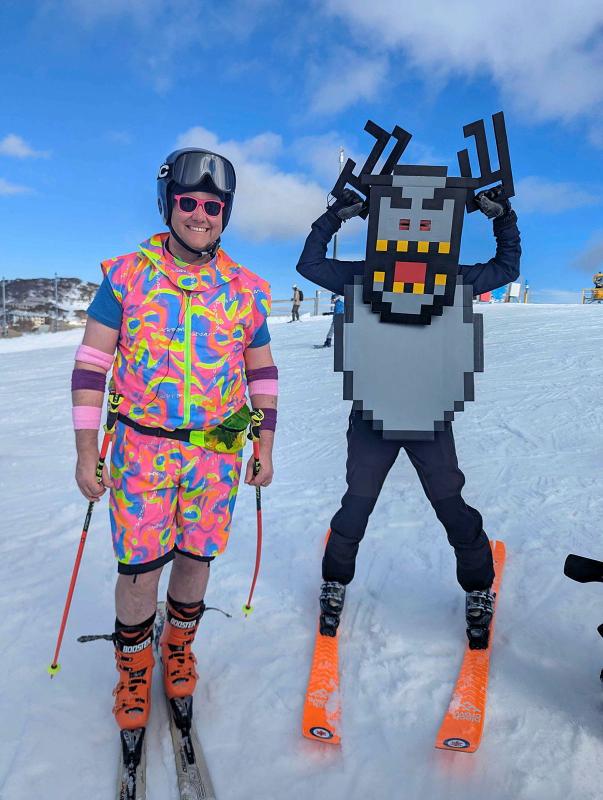 Two people on the snow slopes in funky dress. One is in a rainbow outfit and the other is in a monster costume.