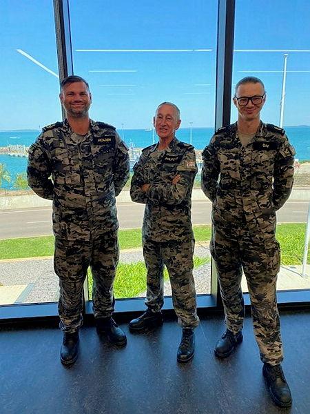 Three Navy officers stand facing the camera and smiling.