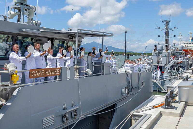 Navy members on the deck of a ship hold their hats in front of them.