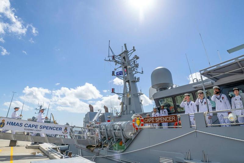 Navy personnel stand on the deck of ship while two others board. 